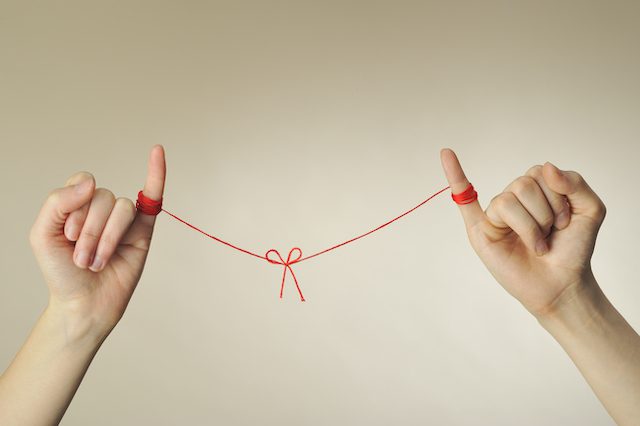 Two people hold out their hands with their pinkies up. Each of their pinkies is wound in red string that is tied in a small bow in the center of the picture. This "pinky promise" represents the commitment that comes with marriage, the topic of discussion for this segment.