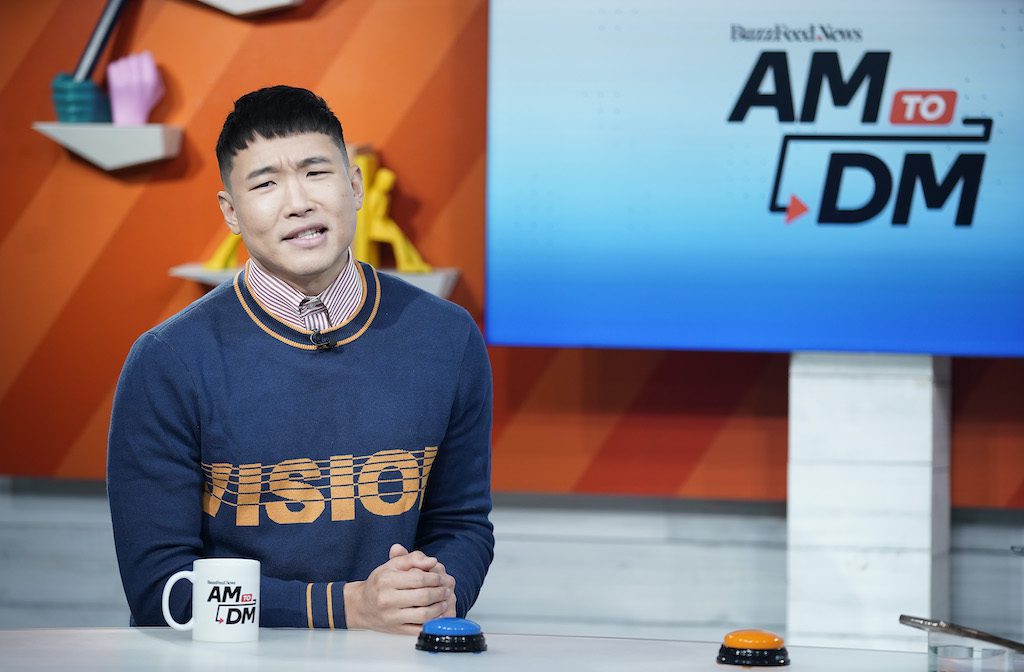 Joel Kim Booster sits behind as desk apparently groaning during his visit to BuzzFeed's "AM To DM" on October 30, 2019 in New York City. 