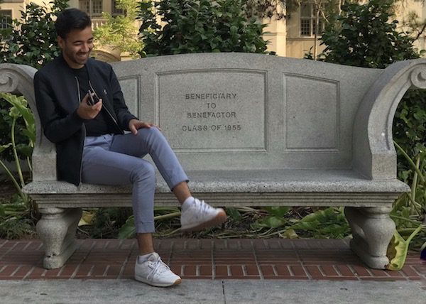 Juan Mireles-Palomar, a gay 21-year-old recipient of DACA (also known as Deferred Action for Childhood Arrivals), sits on a bench smiling as he attempts to cross his legs.