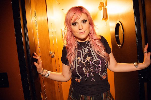 Comedian, music and writer Lane Moore poses in a doorway with both of her hands on the walls around her sides.